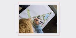 Child drawing on a large map spread on a table, adding stickers and notes with a marker outdoors