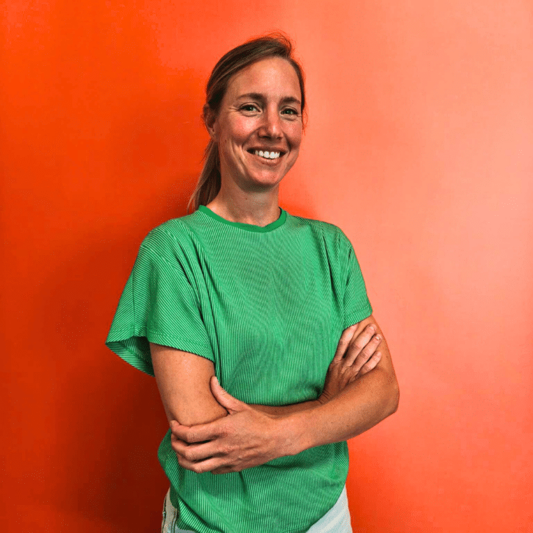 Smiling woman in a green striped T-shirt stands with arms crossed against an orange background.