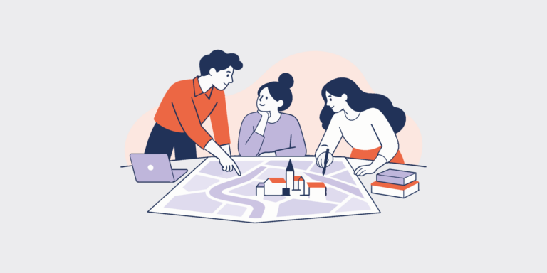 Three people collaborate around a large map plan, with a laptop and building blocks on the table.